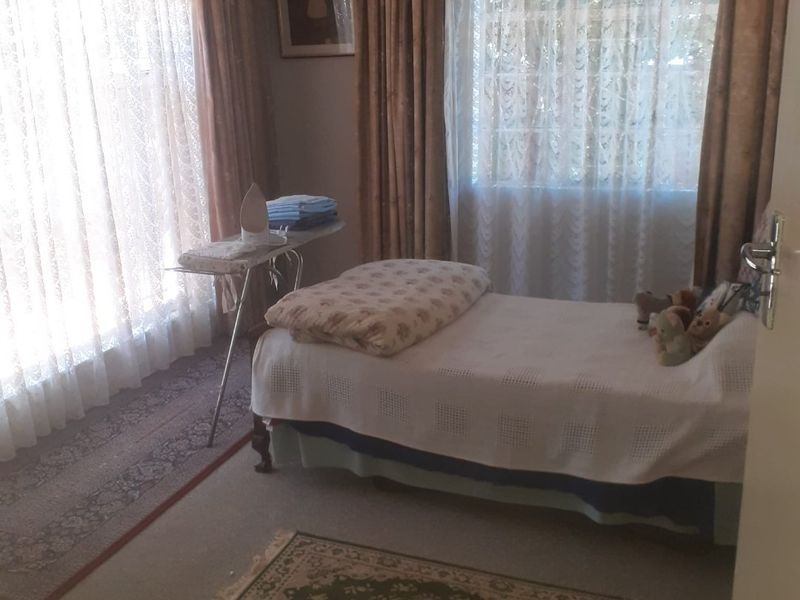 A bedroom featuring carpeted flooring and dual windows with traditional curtain treatments.
