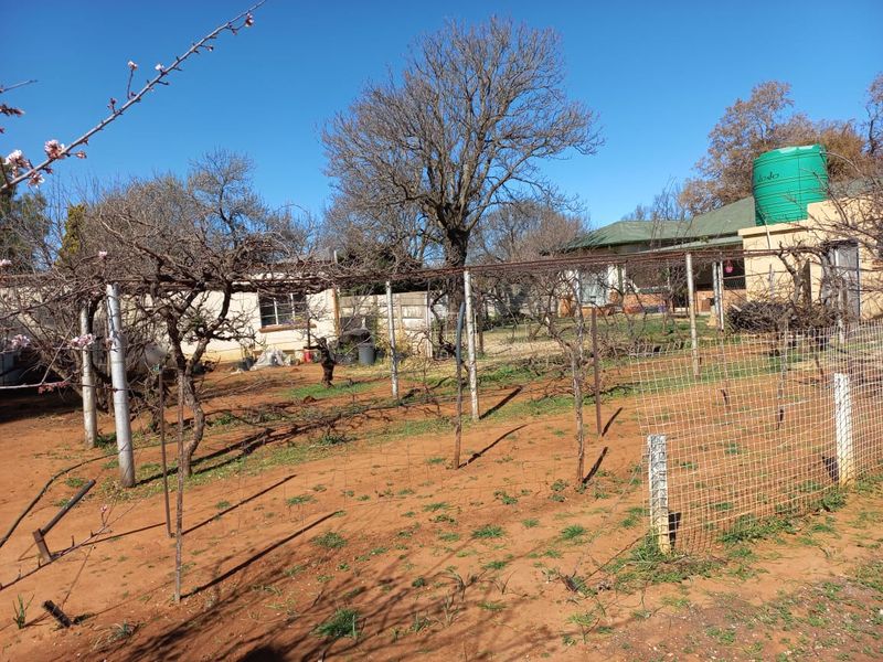 A spacious backyard area featuring a water storage tank, wire fencing, and a trellis structure, offering potential for landscaping and garden development.