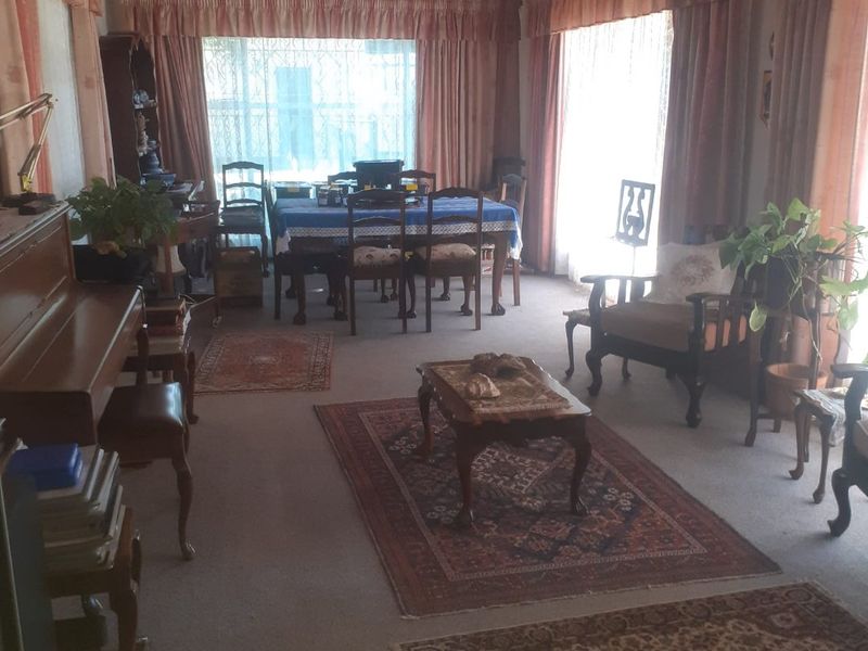 Spacious living and dining area featuring large windows, carpeted flooring, and a timber ceiling, offering a traditional layout with ample natural light.