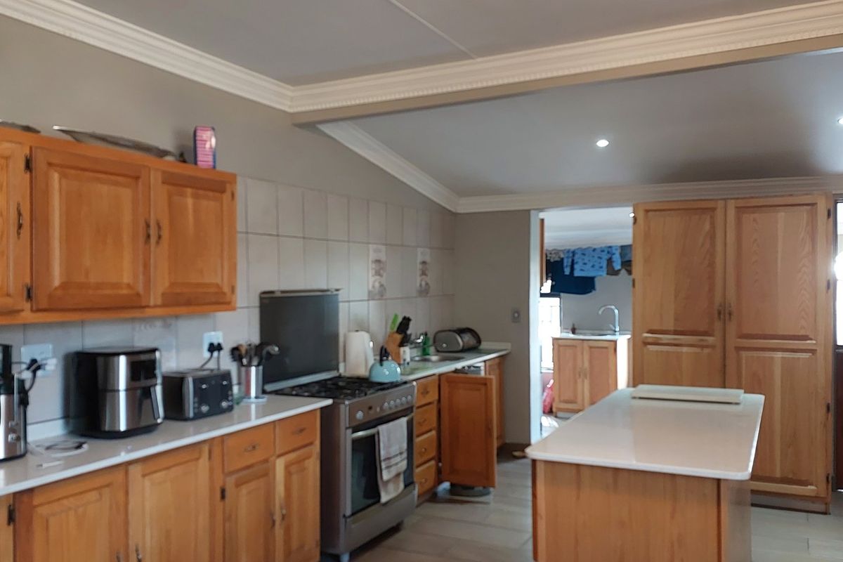 A functional kitchen featuring wooden cabinetry, a gas stove with extractor, and a central island, with a view through to a secondary utility area.