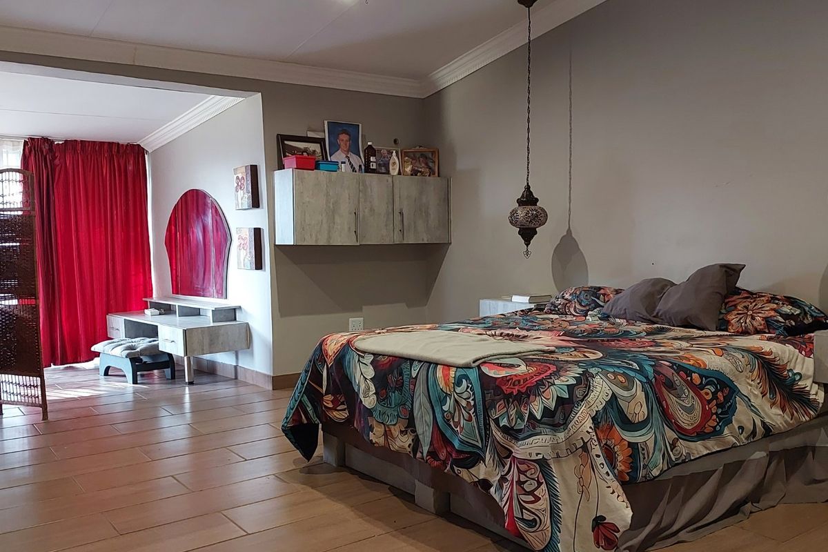 Spacious bedroom featuring tiled flooring, built-in wall cabinetry, and decorative pendant lighting, with an adjoining area currently used as a dressing space.