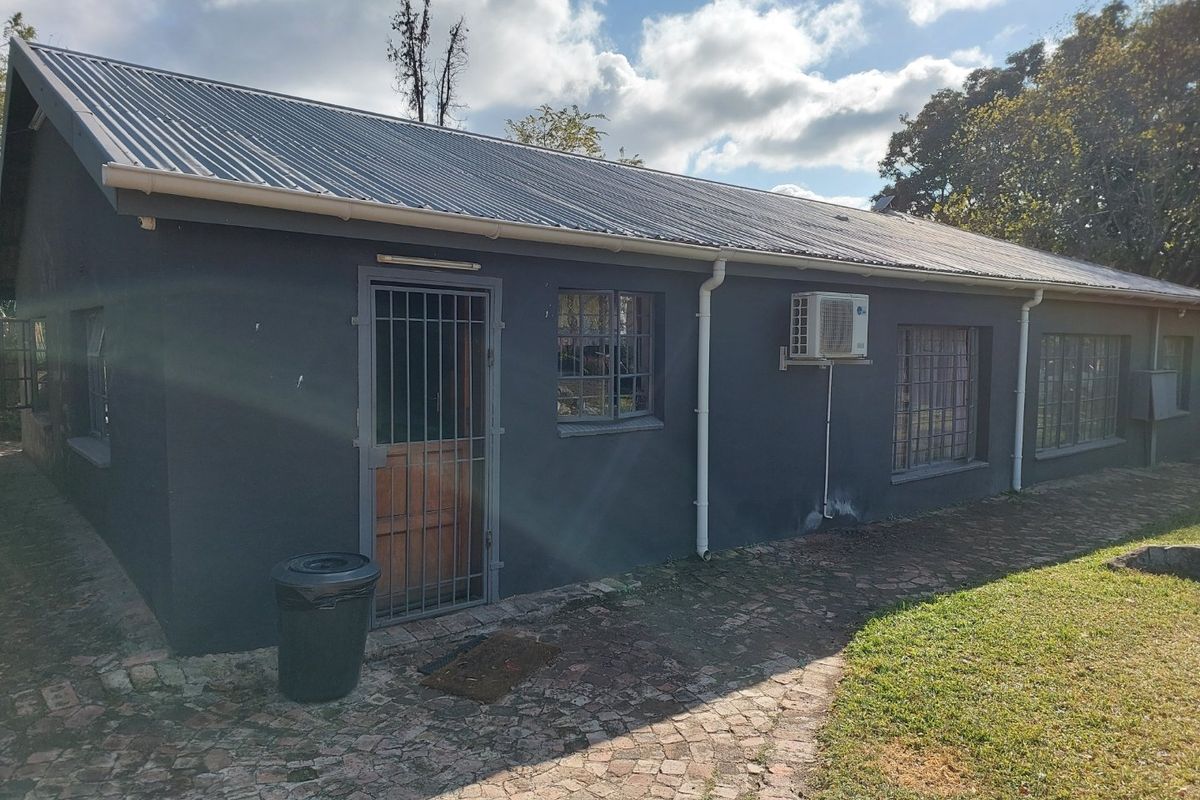 Rear exterior view of the property featuring a corrugated metal roof, security gates, steel-framed windows, and an installed air conditioning unit.