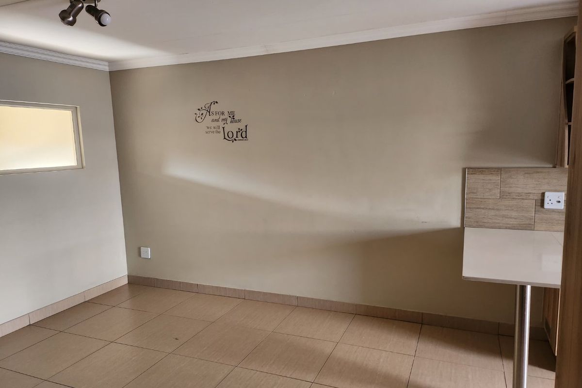 An empty kitchen area featuring tiled flooring, a built-in breakfast bar with tiled splashback, and ceiling-mounted spotlighting.