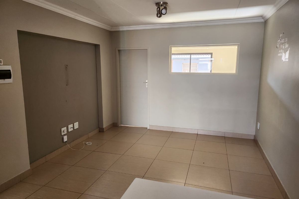 An empty living room featuring neutral tiled flooring, a recessed wall section, and a ceiling-mounted spotlight fixture.