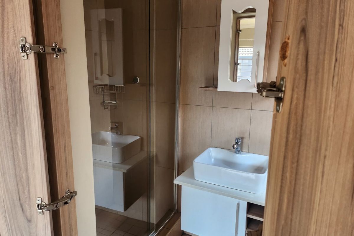 A compact bathroom featuring a glass shower enclosure, a modern vessel sink with a vanity cabinet, and a wall-mounted mirror cabinet.