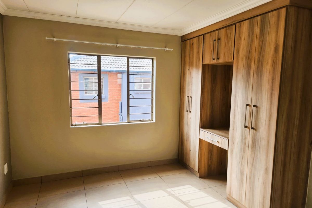 A bright, empty bedroom featuring modern wood-finish built-in cupboards with an integrated vanity and tiled flooring.