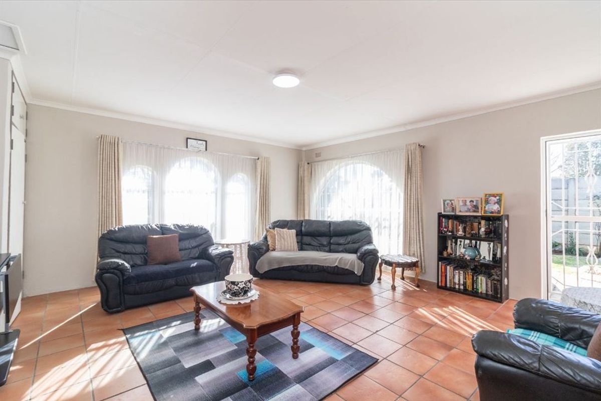 Spacious living room featuring terracotta floor tiles, large arched windows allowing natural light, and direct access to the outdoor area via a security gate.