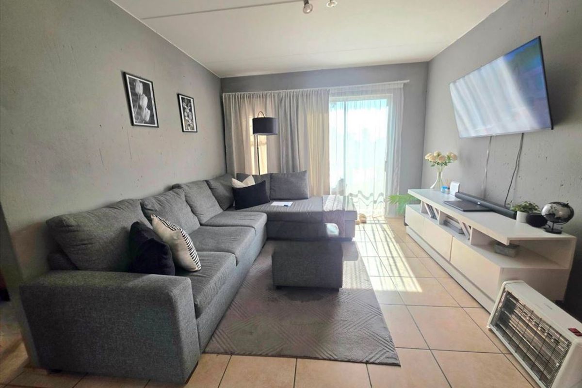 A living room featuring tiled flooring and a sliding glass door providing natural light, with wall-mounted television and neutral grey wall finishes.