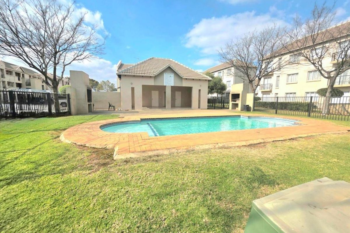 Communal outdoor pool area featuring a swimming pool, brick paving, and built-in braai facilities set within a landscaped garden environment.