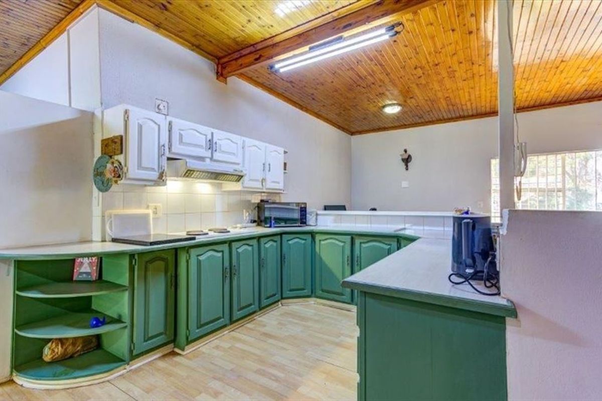 A functional kitchen featuring green and white cabinetry, laminate countertops, a tiled backsplash, and a distinctive timber tongue and groove ceiling.