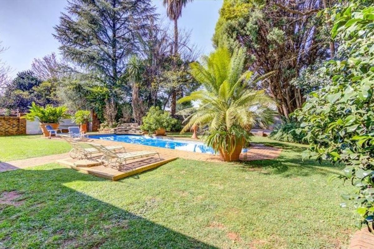 A well-maintained outdoor pool area featuring a swimming pool surrounded by brick paving and established garden landscaping.