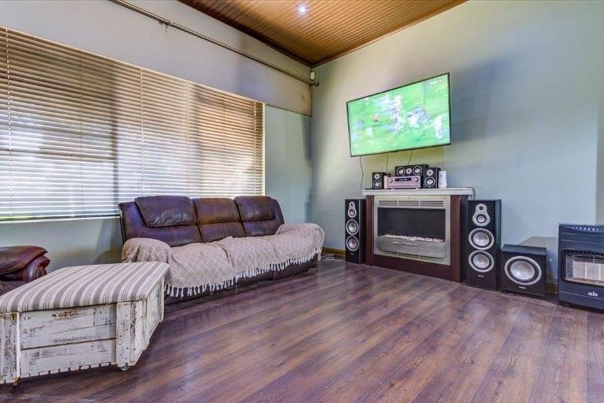 A living room featuring laminate flooring, a timber panelled ceiling, and a built-in fireplace, offering a comfortable and functional space.