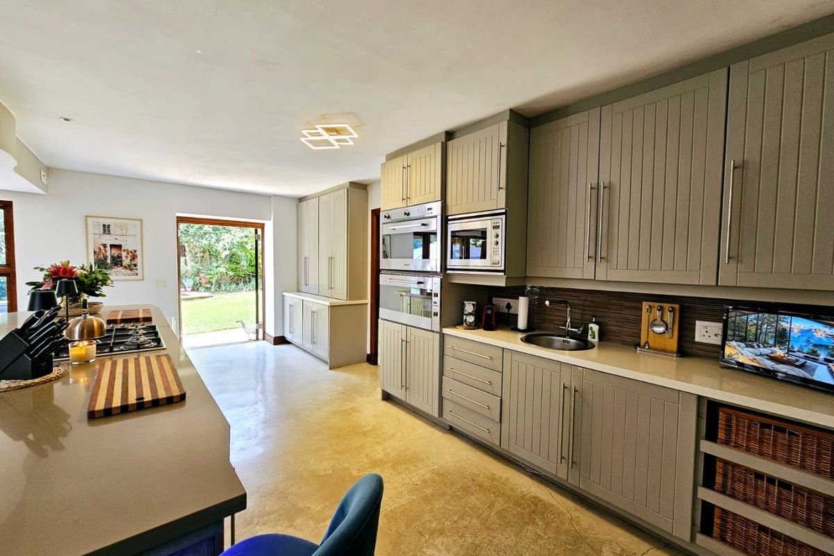 Modern kitchen featuring grey shaker-style cabinetry, stone countertops, integrated appliances, and polished concrete flooring with direct access to the rear garden.