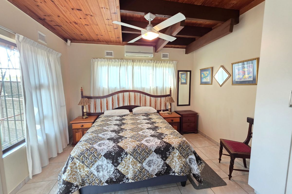 A bedroom featuring exposed timber beam ceilings, tiled flooring, and a wall-mounted split-system air conditioner.