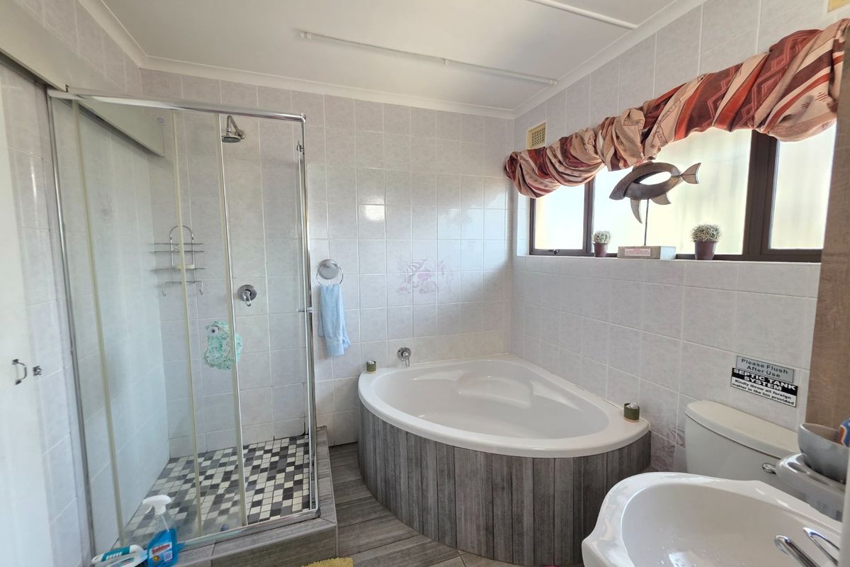 A functional bathroom featuring a corner bathtub, separate glass-enclosed shower, pedestal basin, and tiled finishes throughout.