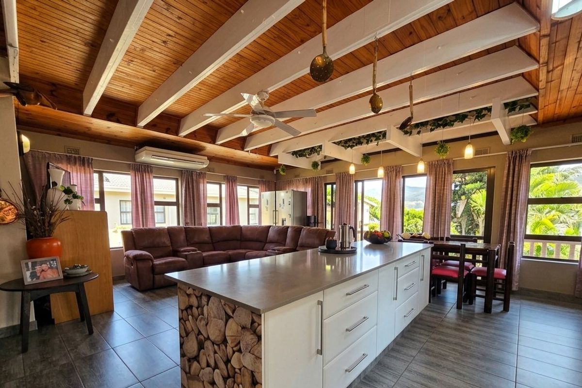 Spacious open-plan living and kitchen area featuring a large central island, exposed timber beam ceilings, and abundant natural light through large windows.