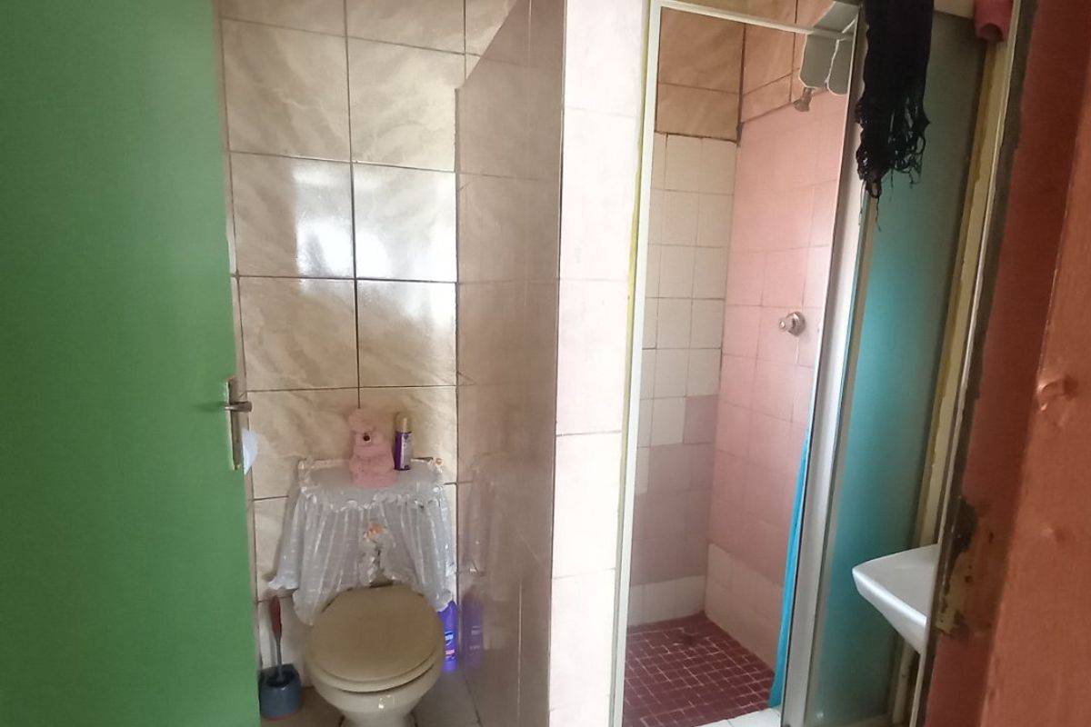 A compact bathroom featuring a shower enclosure, toilet, and wash basin with dated wall tiling and ceiling finishes.