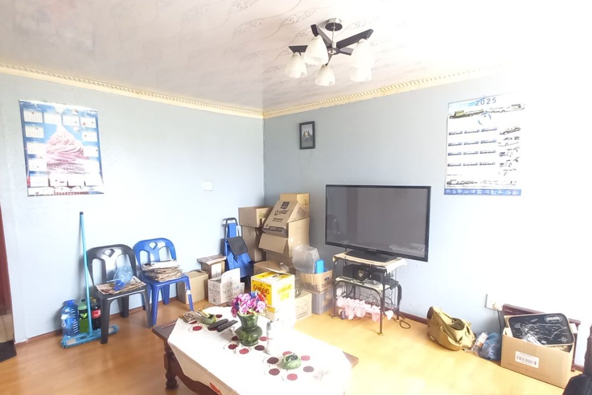 A living room featuring laminate flooring, decorative ceiling coving, and a central multi-arm light fixture, currently showing signs of wear and dated finishes.