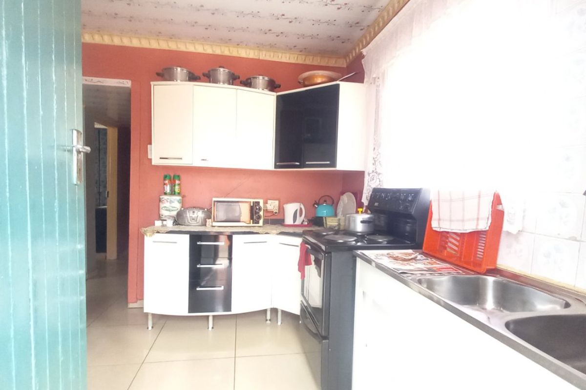 A functional kitchen featuring built-in cabinetry, a double bowl stainless steel sink, and a freestanding stove, with tiled flooring and splashbacks.