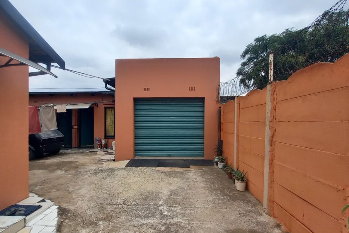 Rear exterior view featuring a concrete driveway, a secure roller shutter garage door, and a high precast boundary wall with security fencing.