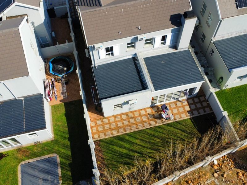 Aerial view of a residential property featuring a tiled roof with solar panels, a paved rear patio, and a private garden area.