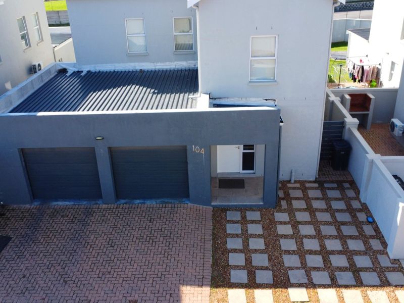 Aerial view of the property entrance featuring a double garage, paved driveway, and a private courtyard area with a built-in braai.