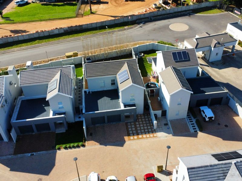 Aerial view of a modern residential complex featuring multiple houses with tiled roofs, solar panels, and paved driveways within a secure estate.