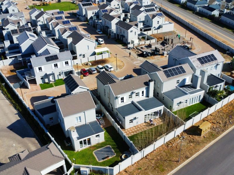 Aerial view of a modern residential estate featuring multiple detached houses with solar panels, private gardens, and paved driveways within a secure complex.
