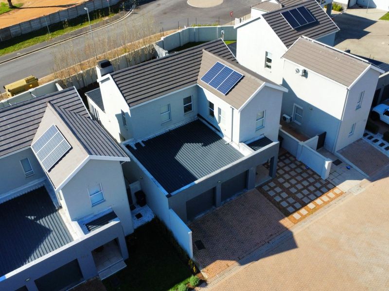 Aerial view of a modern residential property featuring a tiled roof with solar panels, a paved driveway, and an integrated garage.