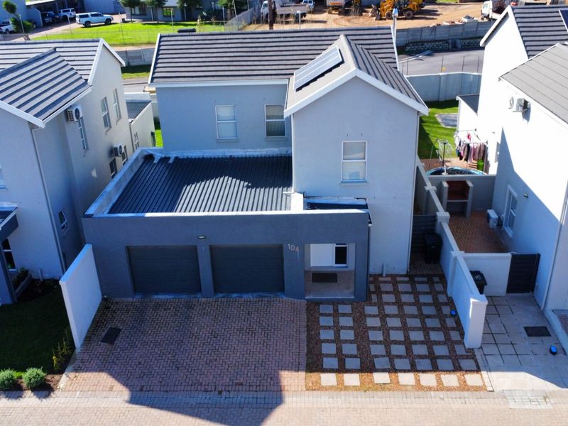 Aerial view of a modern two-story residential property featuring a double garage, paved driveway, and solar panels on the tiled roof.
