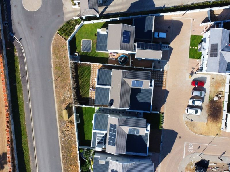 Aerial view of a residential estate showing multiple houses with solar panel installations, paved driveways, and landscaped garden areas.