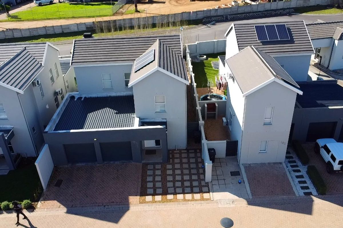 Aerial view of a modern residential property featuring a tiled roof with solar panels, paved driveway, and secure boundary walls.