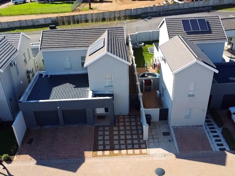Aerial view of a modern residential property featuring a tiled roof with solar panels, paved driveway, and secure boundary walls.
