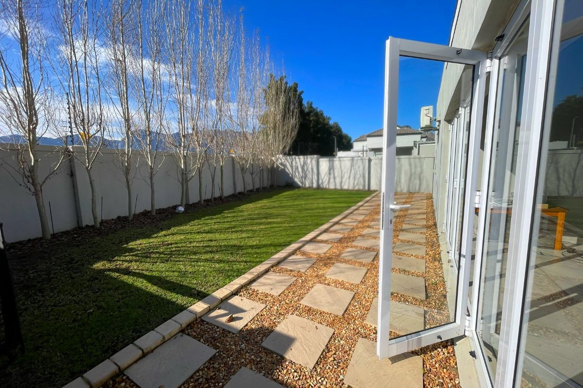 A well-maintained rear garden featuring a paved walkway, gravel landscaping, a neat lawn, and secure boundary walls with electric fencing.