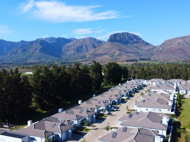 Aerial view of a residential estate featuring uniform housing units with tiled roofs, solar geysers, and mountain views in the background.