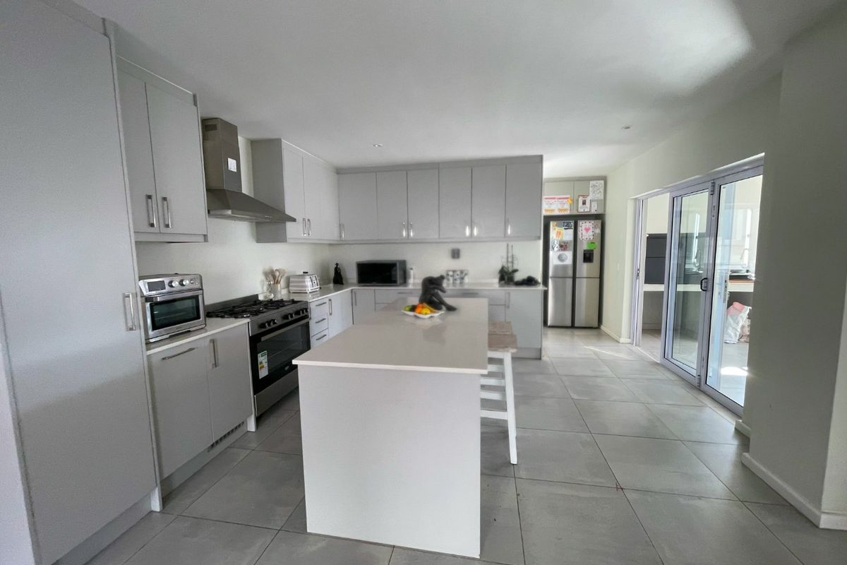 Modern kitchen featuring a central island, quartz countertops, gas hob, built-in oven, and large sliding glass doors leading to the outdoor area.