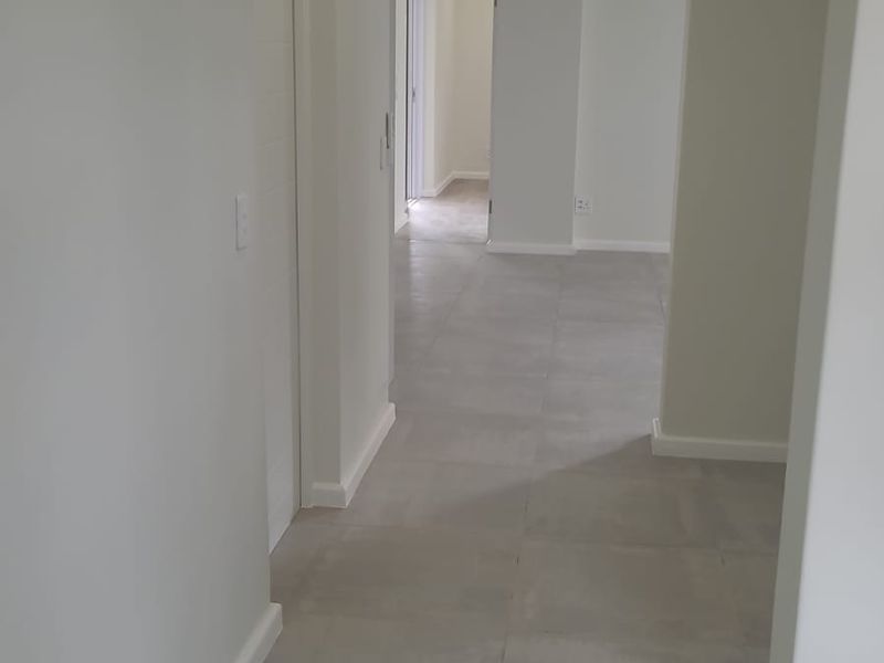 A bright, modern hallway featuring neutral tiled flooring, clean white walls, and recessed downlighting, leading into an open-plan living area.