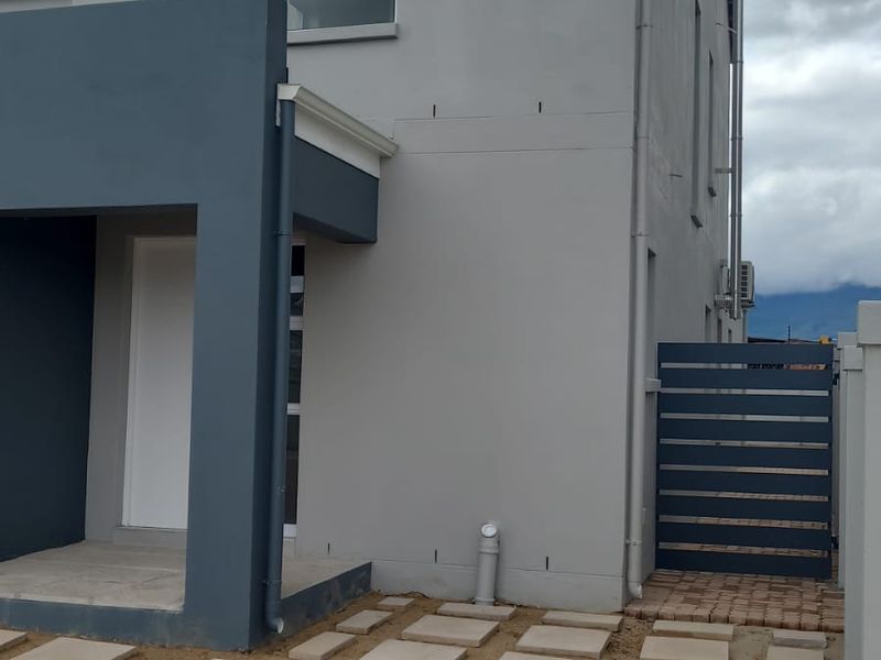 Rear exterior view of a modern two-story house featuring a covered entrance, paved walkway, and side access gate.