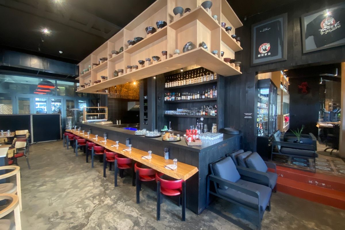 A well-appointed commercial bar area featuring a prominent wooden overhead shelving structure, extensive back bar display, and polished concrete flooring.