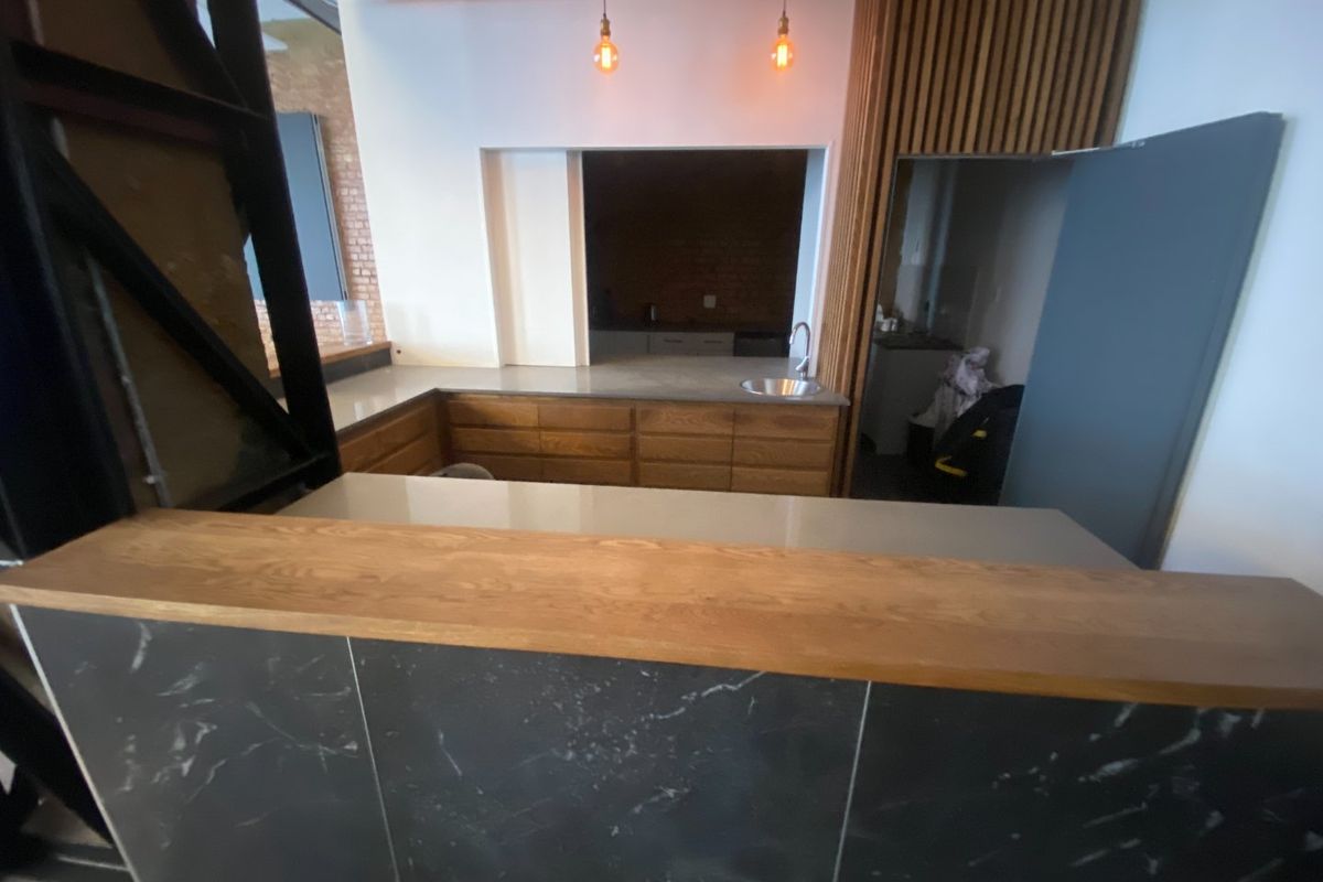 Modern kitchen area featuring timber cabinetry, stone countertops, a breakfast bar, and decorative timber ceiling lattice with pendant lighting.