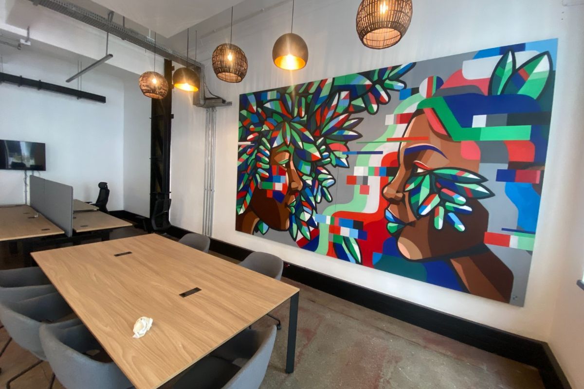 Modern commercial office space featuring exposed industrial ceilings, concrete flooring, and contemporary pendant lighting, accented by a large vibrant wall mural.
