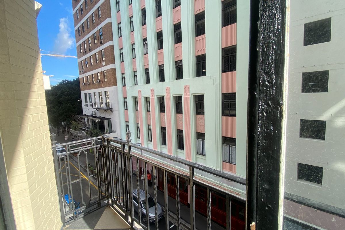 A small balcony with a wrought iron railing overlooking a city street and adjacent historic commercial buildings.