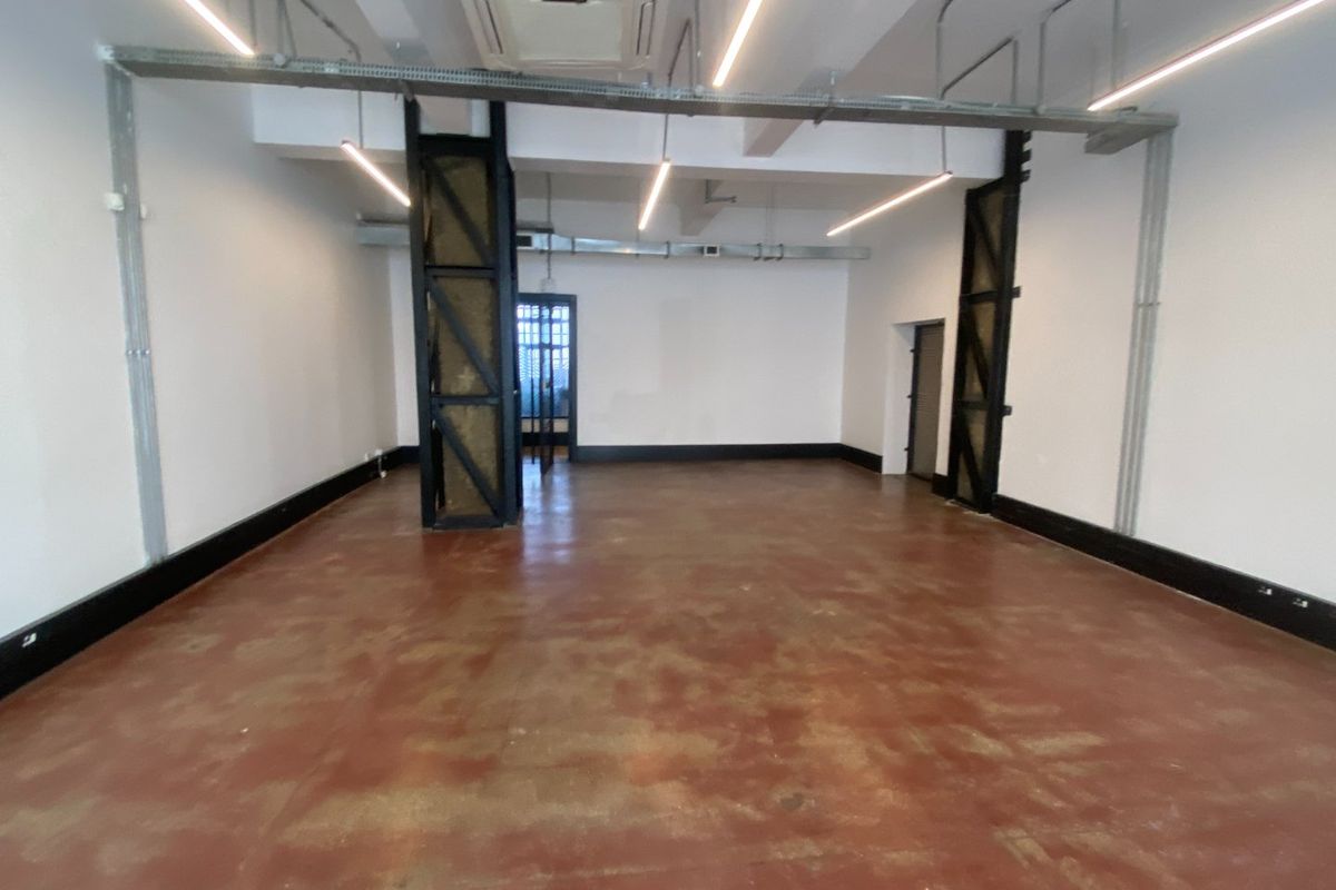 Spacious open-plan commercial area featuring industrial-style exposed ducting, structural steel columns, recessed lighting, and polished concrete flooring.