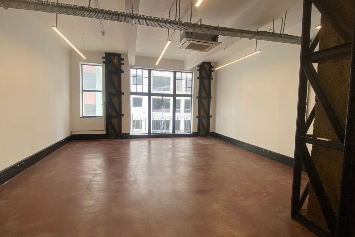 Spacious open-plan commercial office space featuring industrial-style exposed ceilings, polished concrete floors, and large windows providing ample natural light.