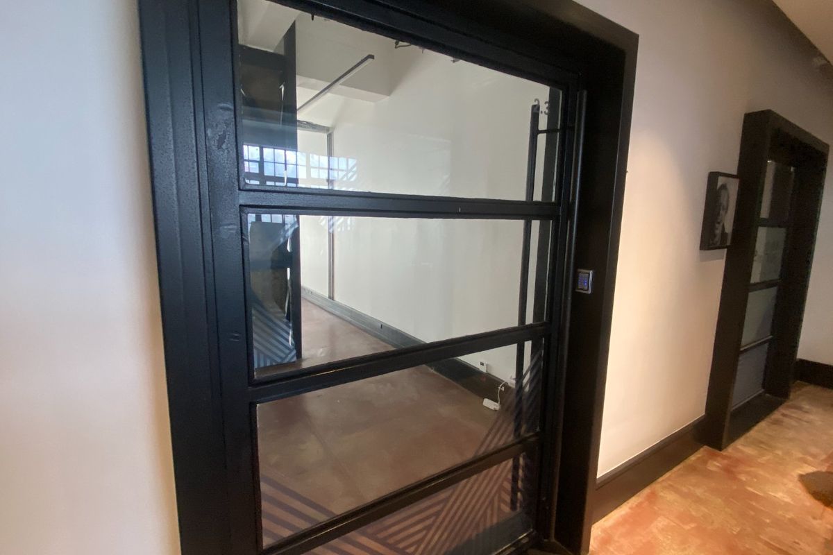 A modern commercial hallway featuring black metal-framed glass doors, electronic access control, and polished hardwood flooring.