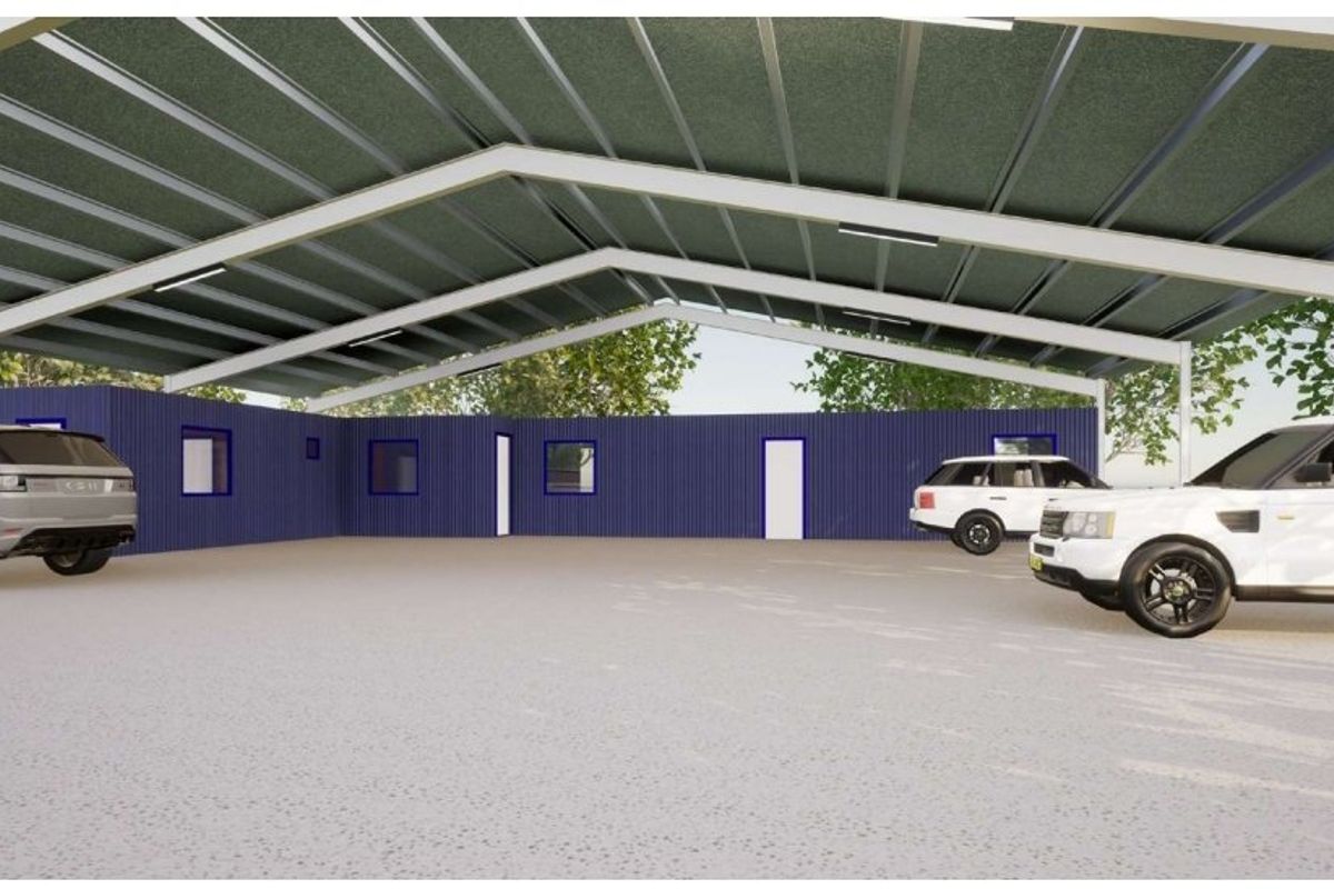 A spacious, modern industrial-style covered parking area featuring a steel portal frame structure, corrugated metal walls, and a durable concrete floor.