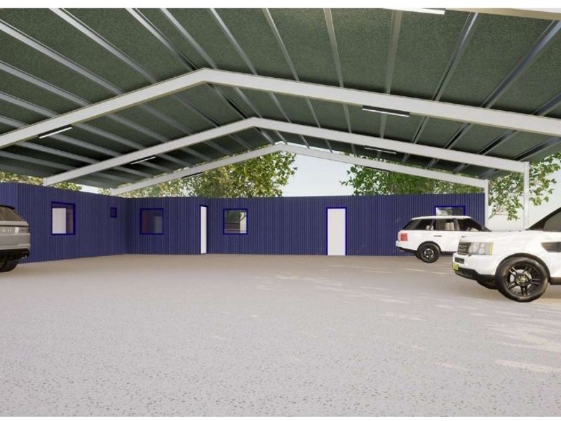 A spacious, modern industrial-style covered parking area featuring a steel portal frame structure, corrugated metal walls, and a durable concrete floor.