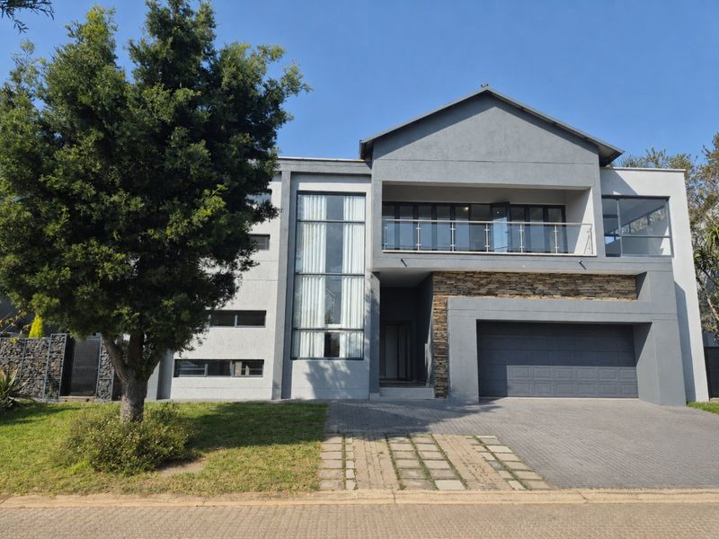 Modern double-story residence featuring a contemporary grey facade, stone cladding accents, a spacious double garage, and an upper-level balcony with glass balustrades.