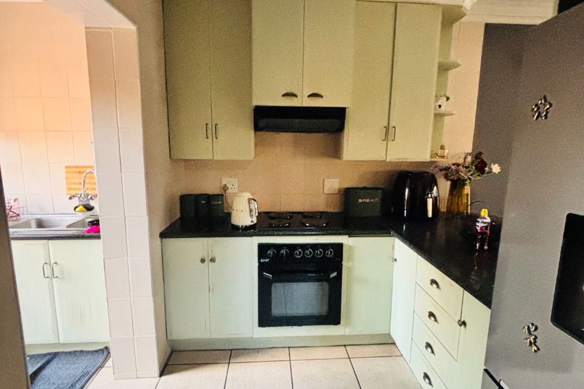 A functional kitchen featuring light-toned cabinetry, built-in oven and hob, tiled flooring, and an adjoining scullery area.