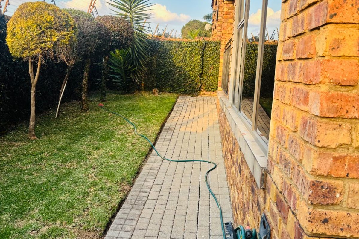 A side view of the townhouse featuring a paved walkway, manicured lawn, and face brick exterior wall with an outdoor water tap.